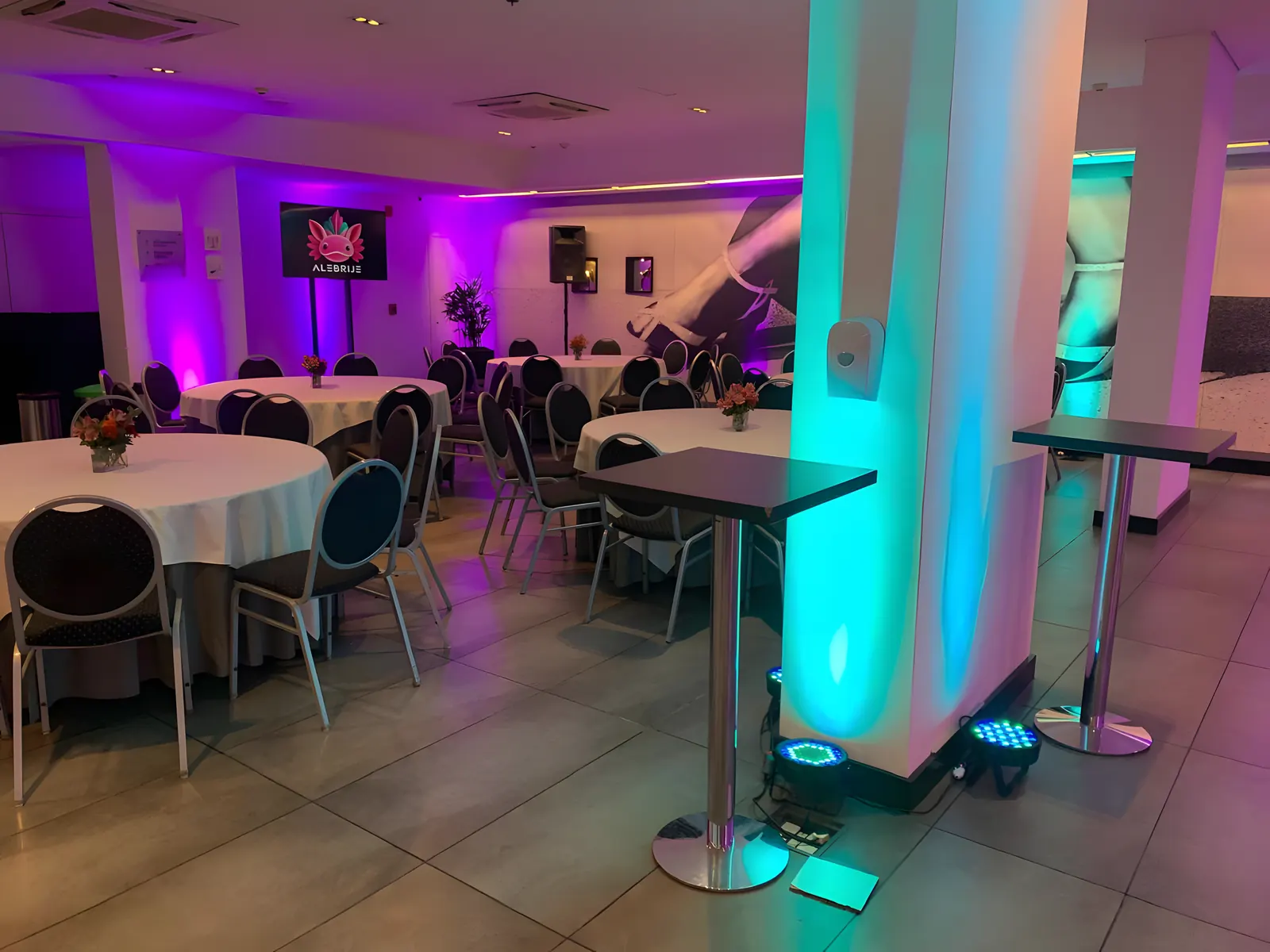 Salón con mesas redondas y una columna iluminada en cian