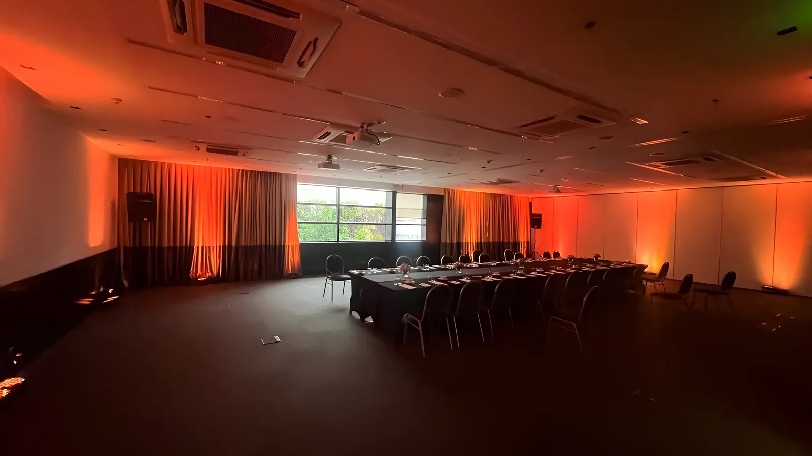Salón con iluminación naranja sobre los cortinados y mesas en U