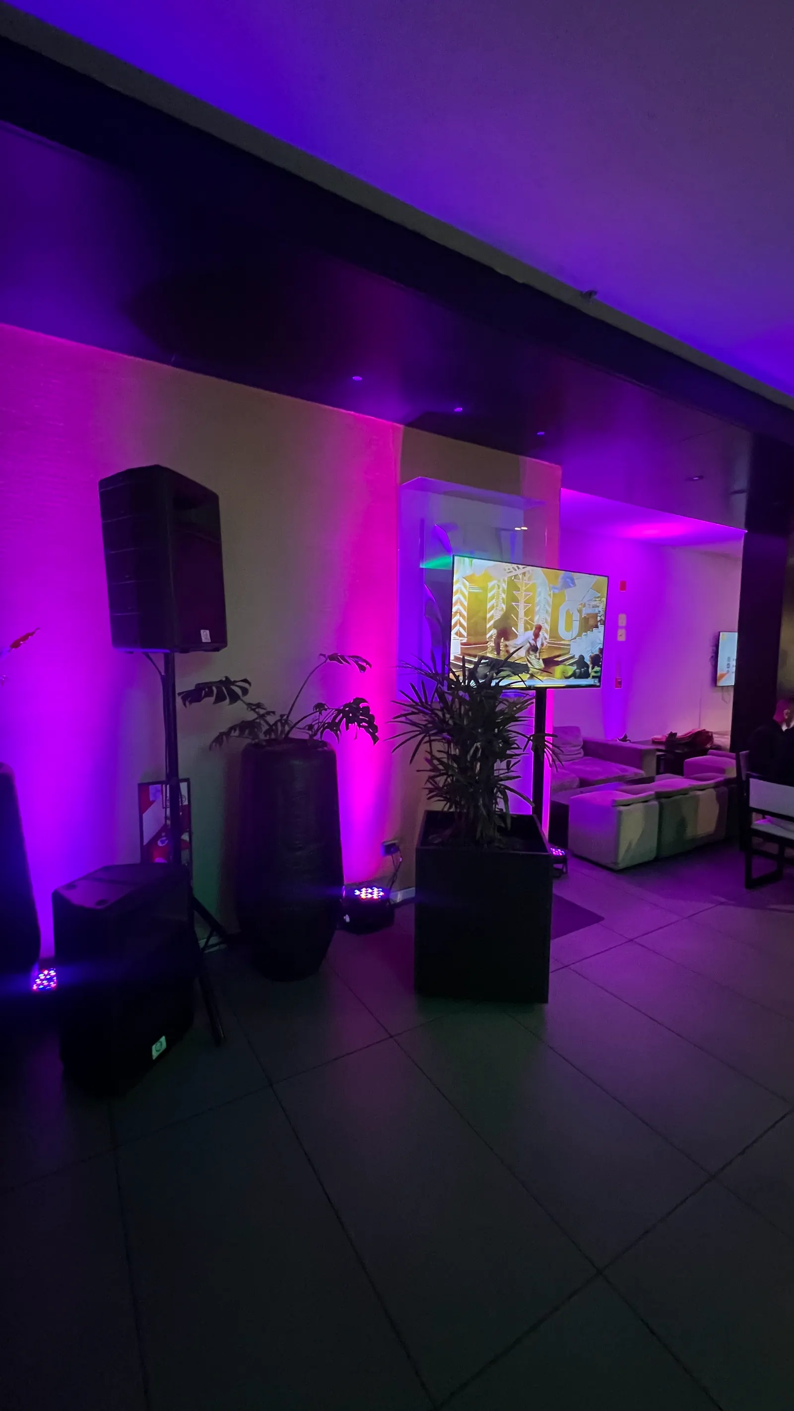 Lounge con luz magenta sobre las paredes, parlantes en trípode y una pantalla