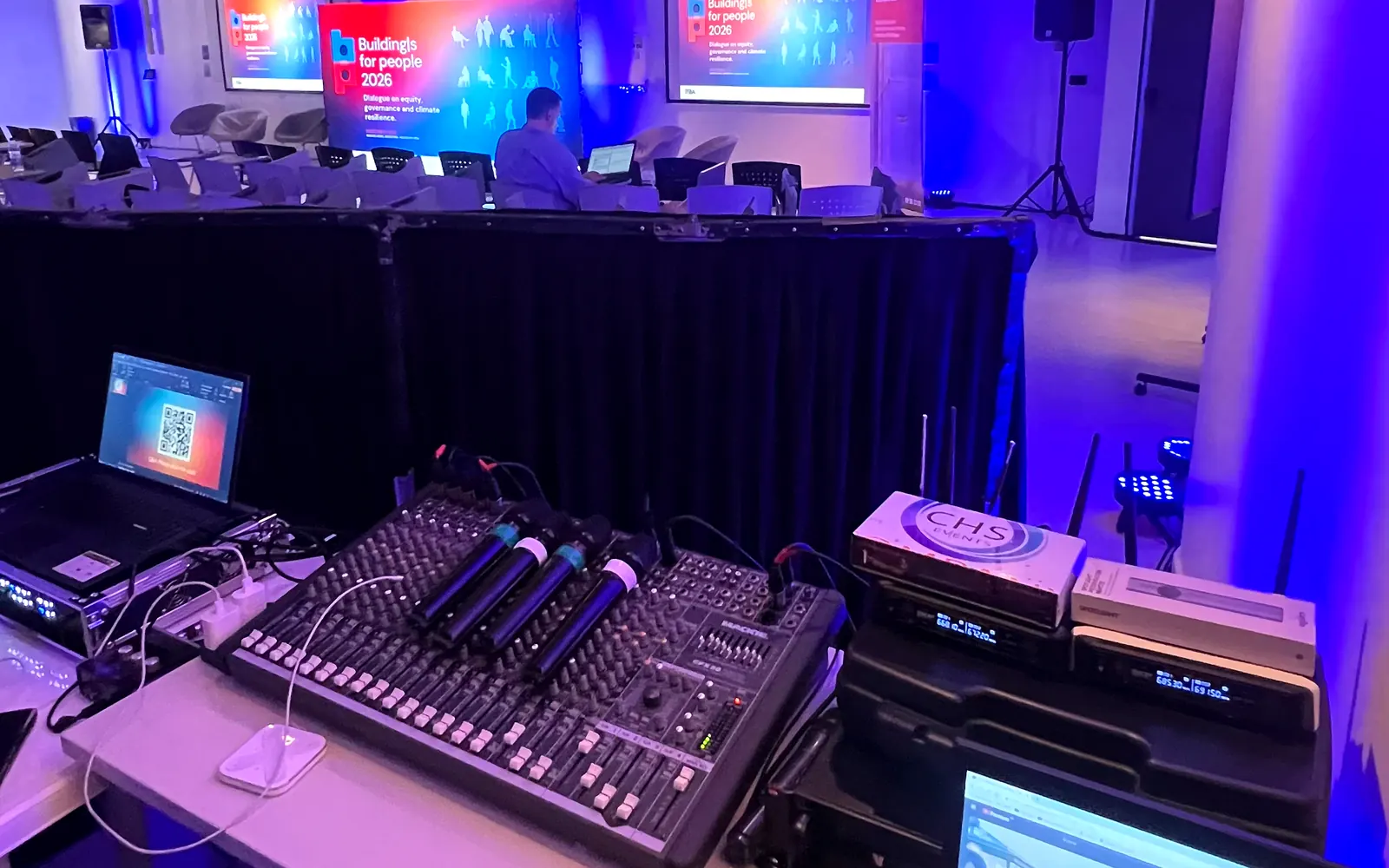Operadores en el puesto de control con notebooks mientras el salón está en plena fiesta