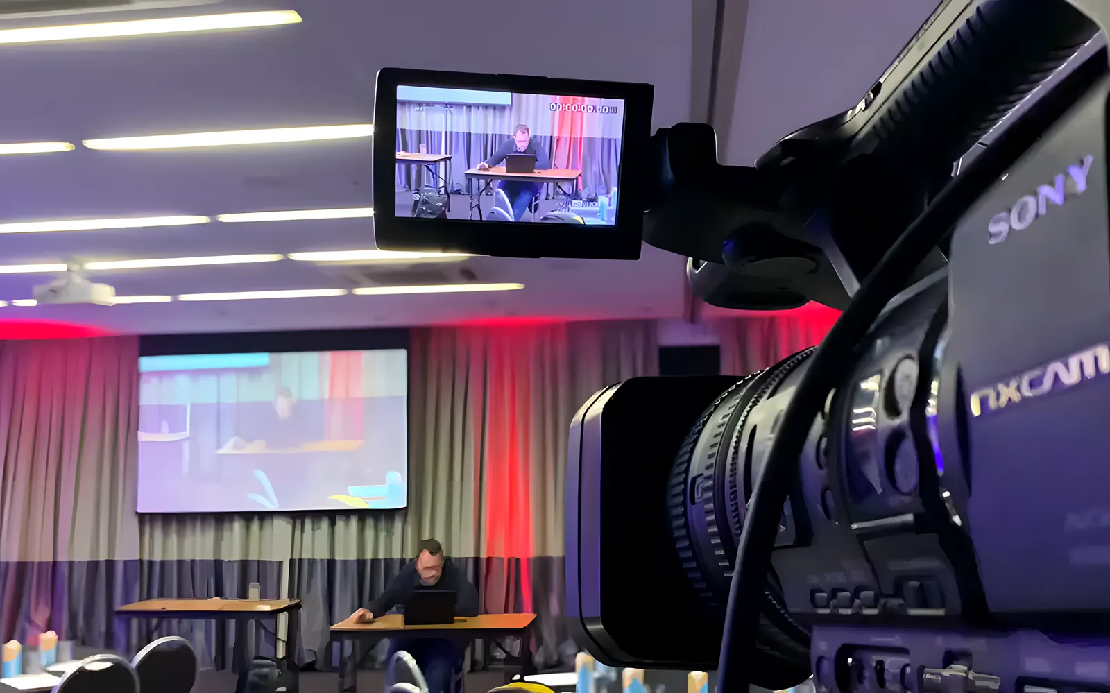 Cámara de video profesional con su monitor grabando un salón con pantalla y orador