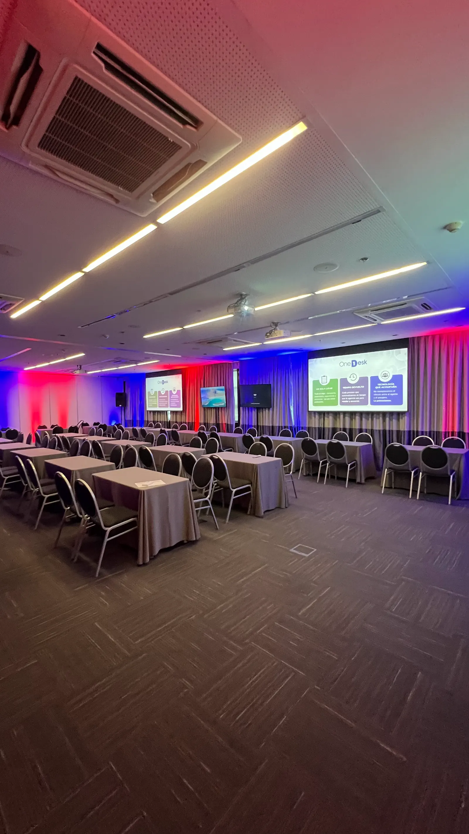 Salón en formato aula con dos pantallas y luz roja y azul sobre las paredes