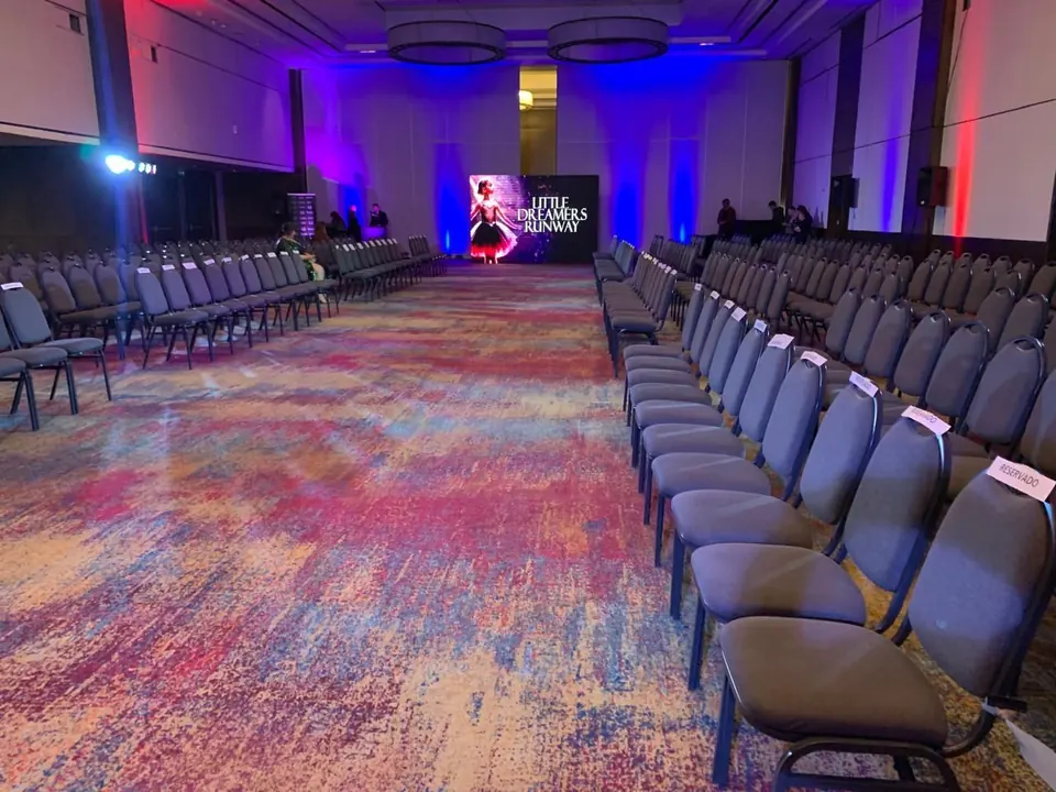 Pasarela con filas de sillas y pantalla LED al fondo